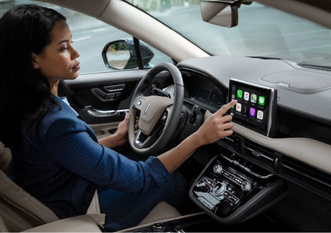 A woman in the driver's seat of a 2022 Lincoln Corsair is touching the center digital screen to connect to Apple CarPlay® | Parkway Lincoln in Dover OH