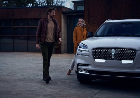 A man and a woman approaching a 2024 Lincoln Aviator® SUV, which illuminates certain lights when they are close | Parkway Lincoln in Dover OH